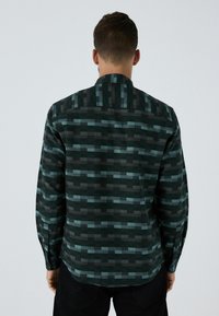 Pitkähihaisen paidan tummanvihreä ja musta kuvio. Siinä on kauluspanta, nappisulkijat ja teksturoitu kangas, jossa on vaihtelevia suorakulmaisia muotoja.