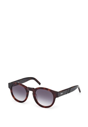 Lunettes de soleil rondes avec un motif écaille de tortue, verres gris dégradés et branches foncées arborant un design texturé subtil.