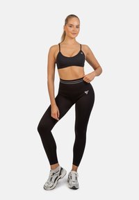 Zwarte sportbh met dunne banden, gecombineerd met hoge zwarte leggings. Sneakers hebben een grijs-wit kleurpatroon.