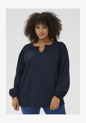 Dunkelblaue Bluse mit V-Ausschnitt und gerafften Details an den Schultern. Lange, voluminöse Ärmel mit elastischen Bündchen und einem lässigen Schnitt.