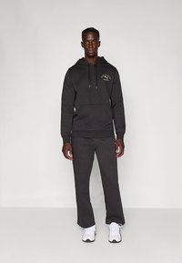 Zwarte katoenen hoodie met trekkoorden, kangoeroezak, gecombineerd met bijpassende broek. Witte sneakers maken de look compleet. Minimalistische ontwerpelementen.