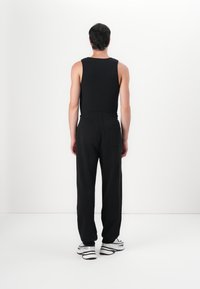 Sort ærmeløs tanktop parret med løse sorte bukser, der har en elastisk talje og en baglomme, set fra bagsiden.