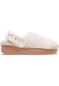 Chaussons blancs pelucheux avec une semelle en caoutchouc beige, design enfilement et accents de boutons sur le côté. La texture douce ajoute du confort.