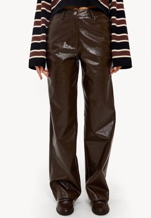 Pantalon large taille haute en similicuir marron porté avec des mocassins marron et un haut à manches longues rayé noir, marron et crème.