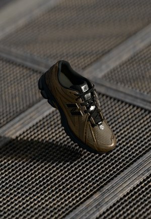 Brune og sorte New Balance sneakers med tekstureret design, sorte snørebånd og logo på metalrist baggrund i naturligt lys.