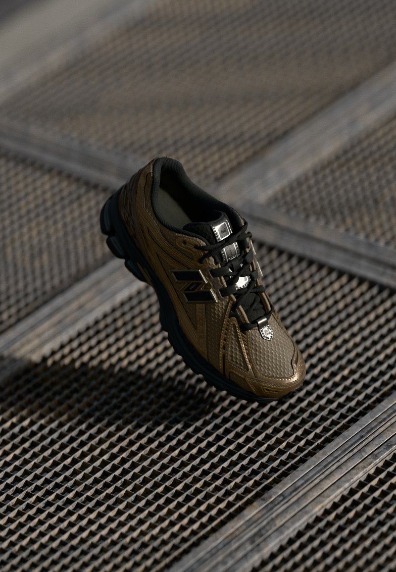 Brown and black New Balance sneaker with textured design, black laces, and logo on metal grate background in natural light.