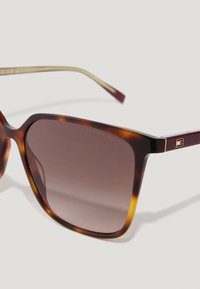 Žlté slnečné okuliare so štvorcovými hnedými gradientovými sklíčkami a tenkými rámami, na ktorých sa nachádza malý zlatý a červený logotyp.