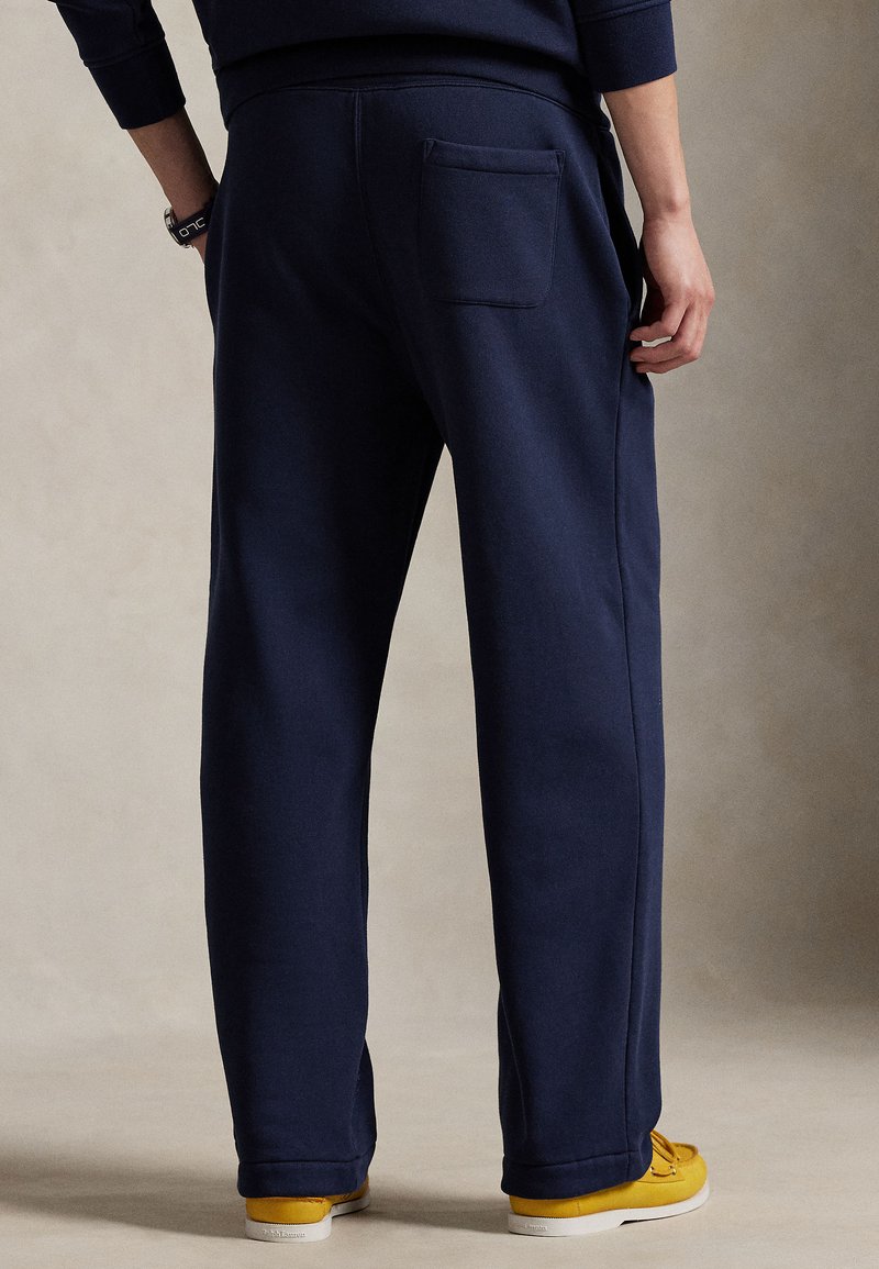 Navy sweatpants with a relaxed fit, featuring a back pocket, elastic waistband, and cuffed ankles. Paired with yellow sneakers.