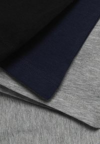 Trois t-shirts en coton empilés : noir, bleu marine et gris clair. Chacun arbore un design simple avec des détails de couture visibles.