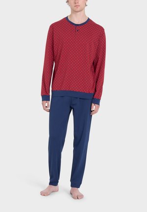 Maglia rossa a maniche lunghe con pois bianchi, polsini blu navy e pantaloni coordinati blu navy. Tessuto morbido, vestibilità rilassata e due bottoni vicino al colletto.