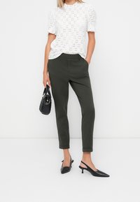 Vit ögla blus med puffärmar, kombinerad med olivgröna tapered byxor, svarta slingback-klackar och en liten svart handväska.