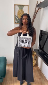 Mustvalge DKNY käekott mustri kujundusega, lühikeste valgete käepidemetega ja eemaldatava õlavarre rihmaga. Kotil on julged tähtedega tekst.
