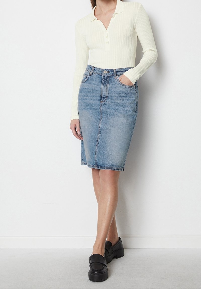 Haut à manches longues crème légèrement ribbé associé à une jupe crayon en denim bleu ajustée avec deux poches avant et une fermeture à bouton.