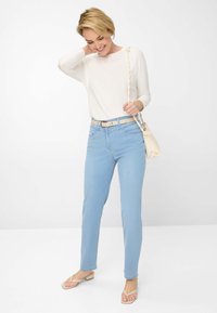Letvægts, langærmet hvid top med rund hals, parret med lyseblå lige jeans og beige flip-flops. Creme farvet crossbody taske.