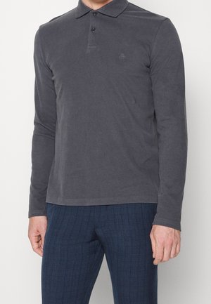 Homme portant un polo à manches longues gris foncé avec trois boutons, associé à un pantalon à carreaux bleu foncé.