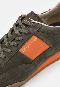 Dunkelgrüner Wildledersneaker mit orangefarbener Applikation, goldener "PS Paul Smith"-Markierung und strukturierten Schnürsenkeln. Gummisohle mit einem Hauch von orange.