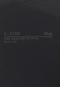 Svart bomullstyg med en mjuk textur som har vit tryckt text: "G-STAR RAW PROD. DEVELOPM. DEPARTM. 18-01/23." Minimalistisk design.