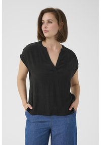 Blouse noire à manches courtes avec un décolleté en V, faite d'un tissu léger. Associée à un pantalon en denim bleu à jambes larges. Texture lisse, coupe décontractée.