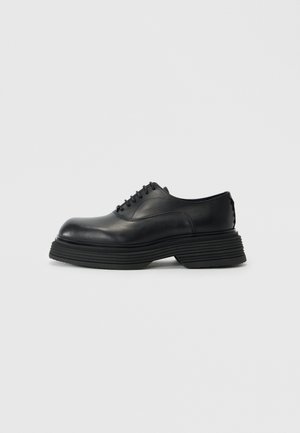Black leather shoes with a rounded toe, featuring a thick layered sole and traditional lace-up design. Smooth texture with minimal detailing.