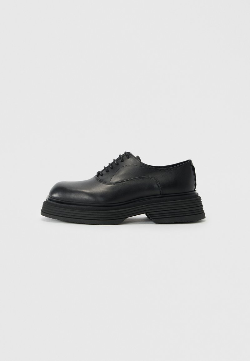 Black leather shoes with a rounded toe, featuring a thick layered sole and traditional lace-up design. Smooth texture with minimal detailing.