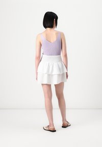 Lyselilla ribbet tanktop med tynne stropper, sammen med en hvit lagdelt skjørt med smock-politik. Sandaler med mørke såler.