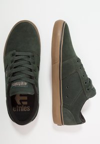 Adidași din suede verde închis cu tălpi din cauciuc maro, având accente și șireturi negre, precum și o talpă interioară personalizată. Design clasic de skate.