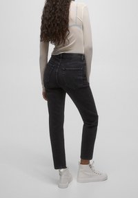 Jean noir taille haute avec une silhouette ajustée et deux poches arrière, associé à des baskets blanches montantes et un haut léger et transparent.