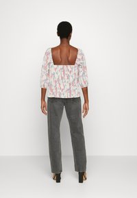 Blusa com padrão floral, costas quadradas e mangas bufantes de três quartos, combinada com jeans cinzentos de cintura alta e pernas retas e sandálias de salto.