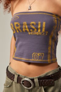 Fialový bezramínkový crop top se žlutým textem "BRASIL" a číslem "07". Má rovný lem a jemnou bavlněnou texturu. Viditelný hnědý opasek se cvočky.