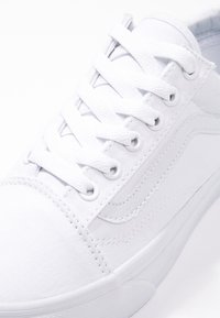 Sneaker bianco in tela con punta tonda, lacci bianchi piatti, occhielli metallici e dettaglio a striscia laterale. Texture liscia e design minimalista.