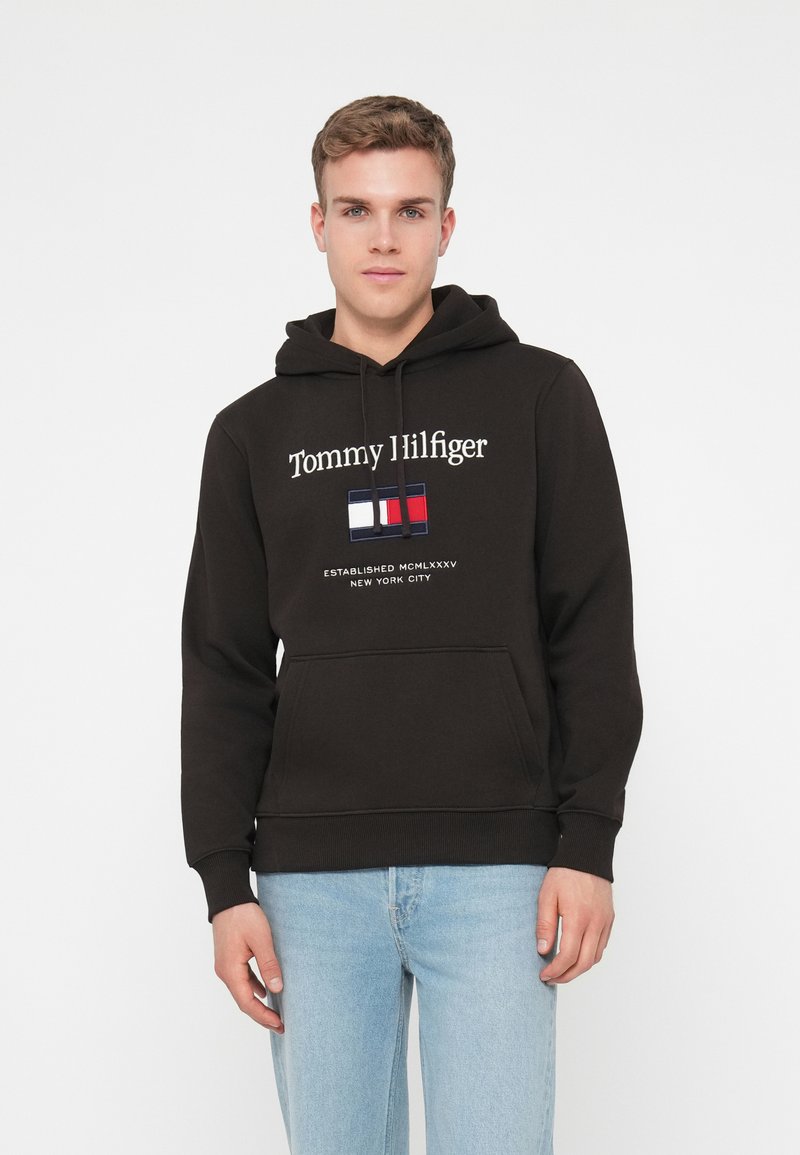 Felpa nera in cotone; presenta il testo "Tommy Hilfiger" in bianco e un logo tricolore. Ha una tasca a marsupio e polsini a costine.