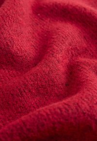 Červená textúrovaná látka s mäkkým, chlpatým vzhľadom, zobrazujúca vzor tkania a rôzne odtiene červenej a čiernej po celej ploche.