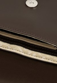 Interior de un bolso de cuero marrón con un cierre de presión plateado. Incluye compartimentos con forro beige y estampado, con un detalle de cremallera.