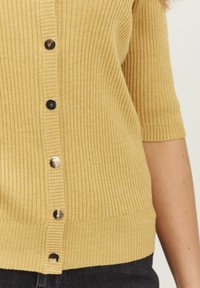 Ribbede sennepsgule cardigan med korte ærmer, der har en knaplukning fortil og skinnende sorte knapper. Blødt, tekstureret stof.