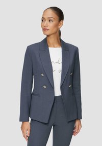 Blazer ajusté bleu foncé à double boutonnage avec des accents de boutons dorés, revers à cran et poches latérales, porté sur un tee-shirt graphique blanc.