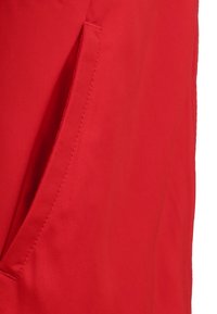Rote Baumwolljacke mit seitlicher Tasche und sichtbaren Nähten, die eine glatte Textur aufweist und einfache, funktionale Designelemente präsentiert.