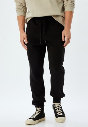 Sorte sweatpants med elastisk talje og snor. Lavet af blødt stof, tætsiddende pasform, med ribbede manchetter og sidelommer.