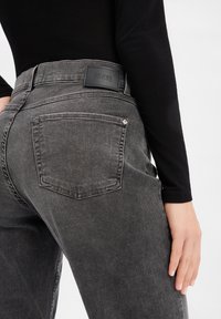 Jeans en denim gris avec une texture lisse, une taille haute, des poches arrière visibles et une étiquette de marque noire sur la ceinture.