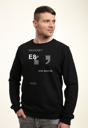 Felpa nera con collo tondo, caratterizzata da testo grigio: "HACKNEY E8" e "'STAY SURREAL'" sulla parte anteriore, realizzata in tessuto morbido.