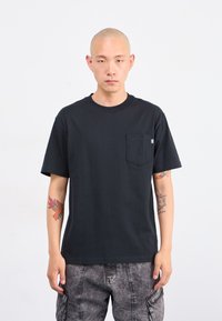 T-shirt en coton noir avec un col rond et des manches courtes, doté d'une poche sur la poitrine. Le tissu semble lisse avec une coupe décontractée.
