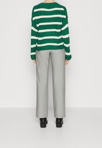 Maglione lavorato a maglia a righe verdi e bianche con una vestibilità comoda, abbinato a pantaloni grigi chiari su misura e stivali neri alla caviglia.