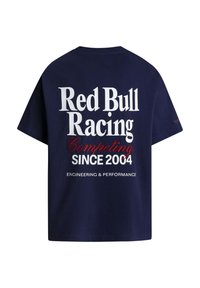 Tengerészkék póló, amelynek hátulján fehér és piros betűkkel a "Red Bull Racing Competing Since 2004 Engineering & Performance" felirat olvasható.