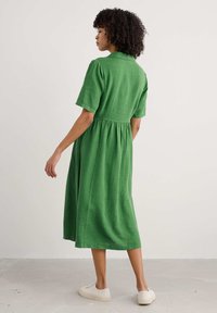 Rochie din in verde, cu guler, mâneci scurte și talie strânsă, care ajunge până la jumătatea gambei. Caracterizată de un material texturat și un design simplu.