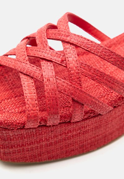 Κόκκινο υφασμάτινο σανδάλι πλατφόρμας με σταυρωτά λουριά και υφασμένη σόλα, εμφανιζόμενο σε κοντινό πλάνο πάνω σε λευκό φόντο.