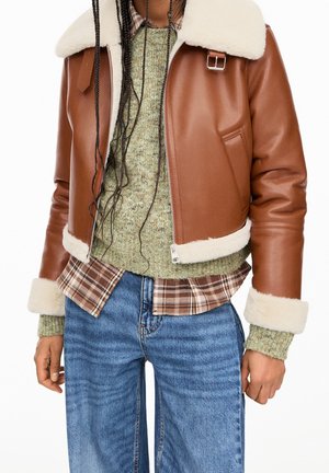 Brown leather jacket with white shearling collar and cuffs over green knit sweater and brown plaid shirt, paired with blue jeans.