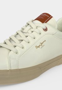 Αθλητικό παπούτσι Pepe Jeans London σε απόχρωση εκρού με μπεζ σόλα, λευκά κορδόνια και καφέ επωνυμία στη γλώσσα.