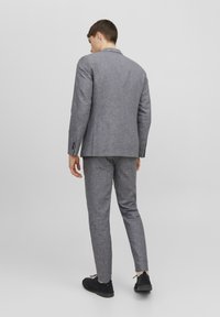 Completo grigio da uomo realizzato in un tessuto texturizzato, con giacca su misura e pantaloni slim-fit, abbinato a scarpe nere.