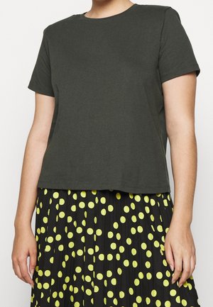 Kobieta ubrana w gładką ciemnoszarą koszulkę z krótkim rękawem w połączeniu z czarną spódnicą w jasne żółte kropki.