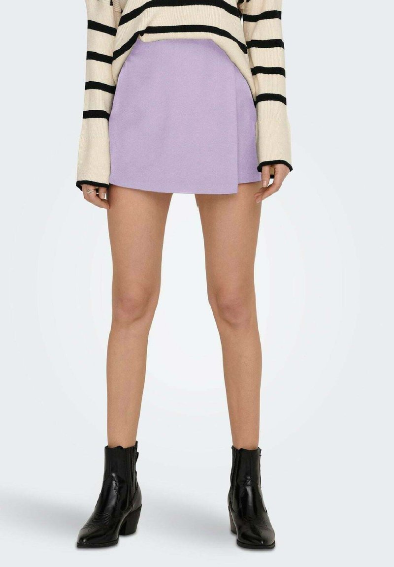 Mini gonna lilla realizzata in un tessuto morbido, con design avvolgente. Abbinata a stivaletti neri alla caviglia con una finitura testurizzata e tacco a strati.