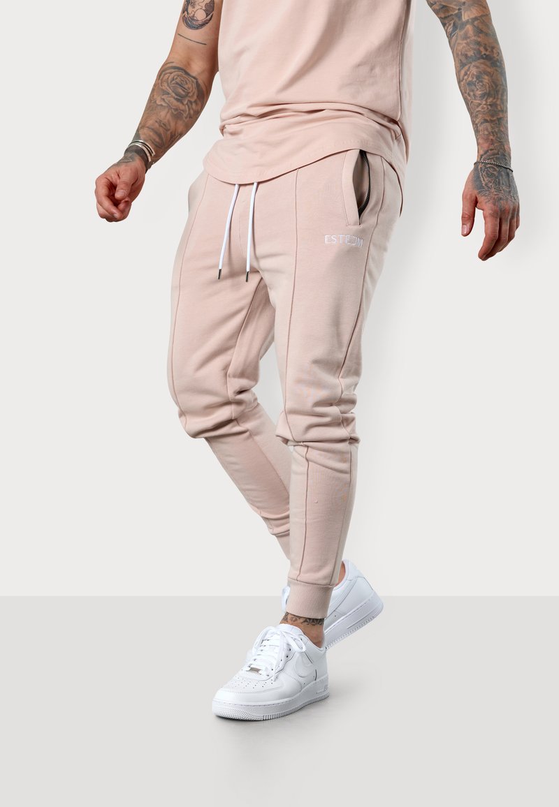 Helle rosa Jogginghosen mit seitlichen Taschen und Kordelzug. Mit weißen Logo-Details und tonal abgesteppten Nähten. Kombiniert mit weißen Sneakers.